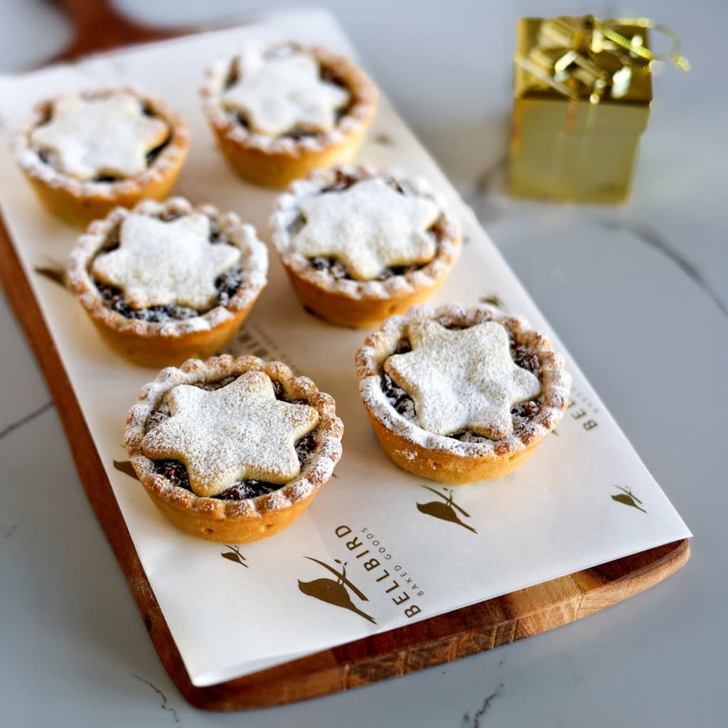 Six fruit mince tarts on a wooden board with Bellbird Bakery paper underneath