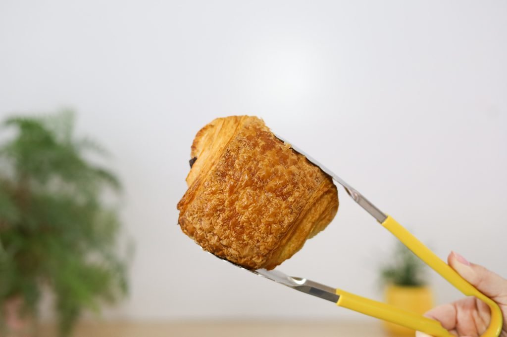 French Pain au Chocolat Bellbird Bakery held with yellow tongs