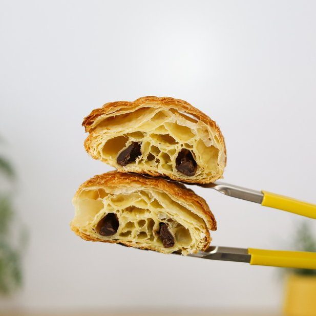 Pain au chocolat cut in half held by yellow tongs at Bellbird Bakery Christchurch