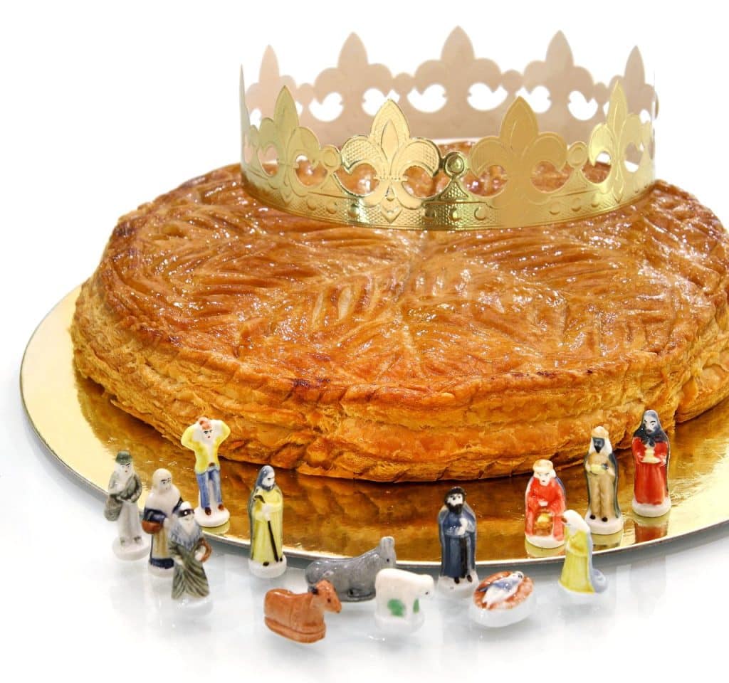 Galette des rois with paper crown and Nativity fèves on a white background
