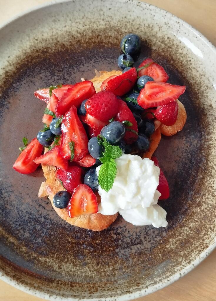 Vegan croissant with strawberries and blueberries, mint, yoghurt and maple syrup on brown plate