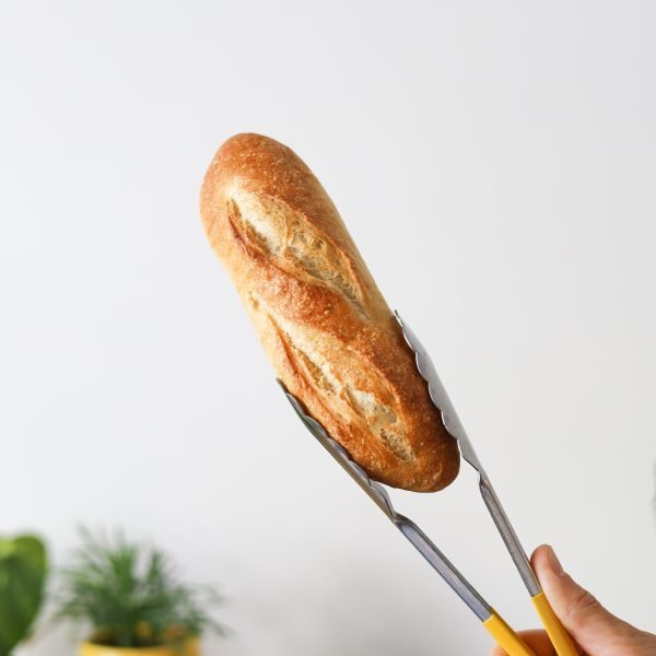 Mini baguette held with tongs against white wall
