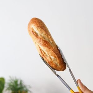 Mini baguette held with tongs against white wall