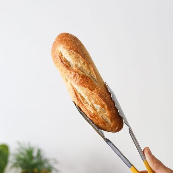 Mini baguette held with tongs against white wall