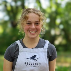 Alice V smiling at the Riccarton Bush farmers market with Bellbird Baked Goods grey apron