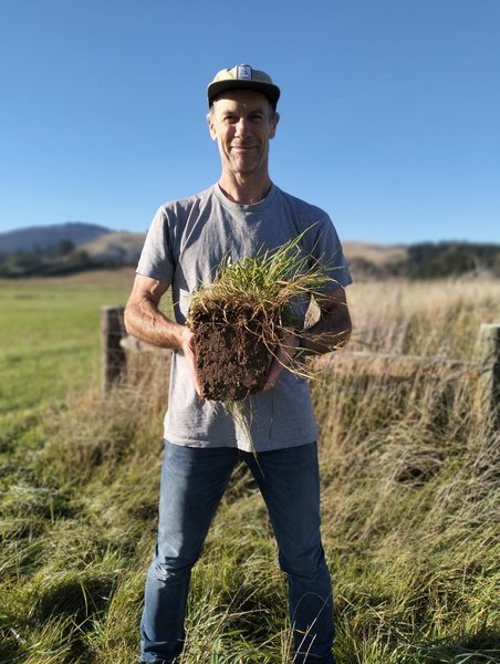 Dave from Bellbird Bakery standing and holding a piece of soil on a sunny regenerative farm