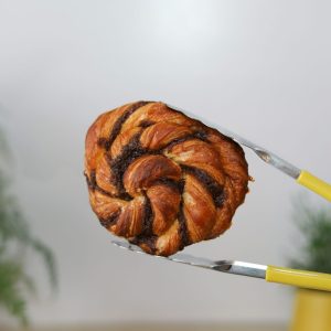 Cinnamon knot pastry held by yellow tongs at Bellbird Bakery