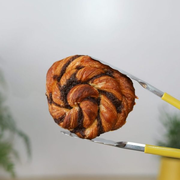 Cinnamon knot pastry held by yellow tongs at Bellbird Bakery