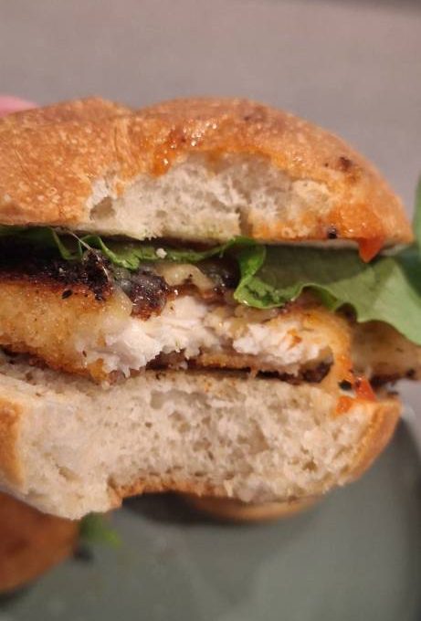 A half-eaten crumbed chicken burger with lettuce and tomato sauce on a Bellbird Bakery focaccia bun