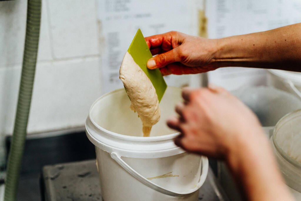 Sourdough starter being weighed up in white bucket with dough cutter
