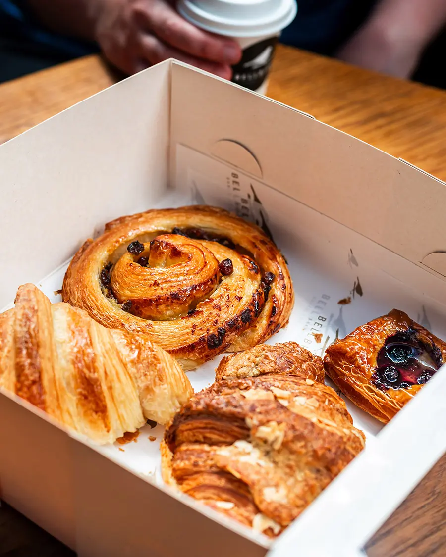 The Classic Box with hands grabbing pastries with Croissant, Pain Aux Raisins, Almond Croissiant and Mini Fruit Danish
