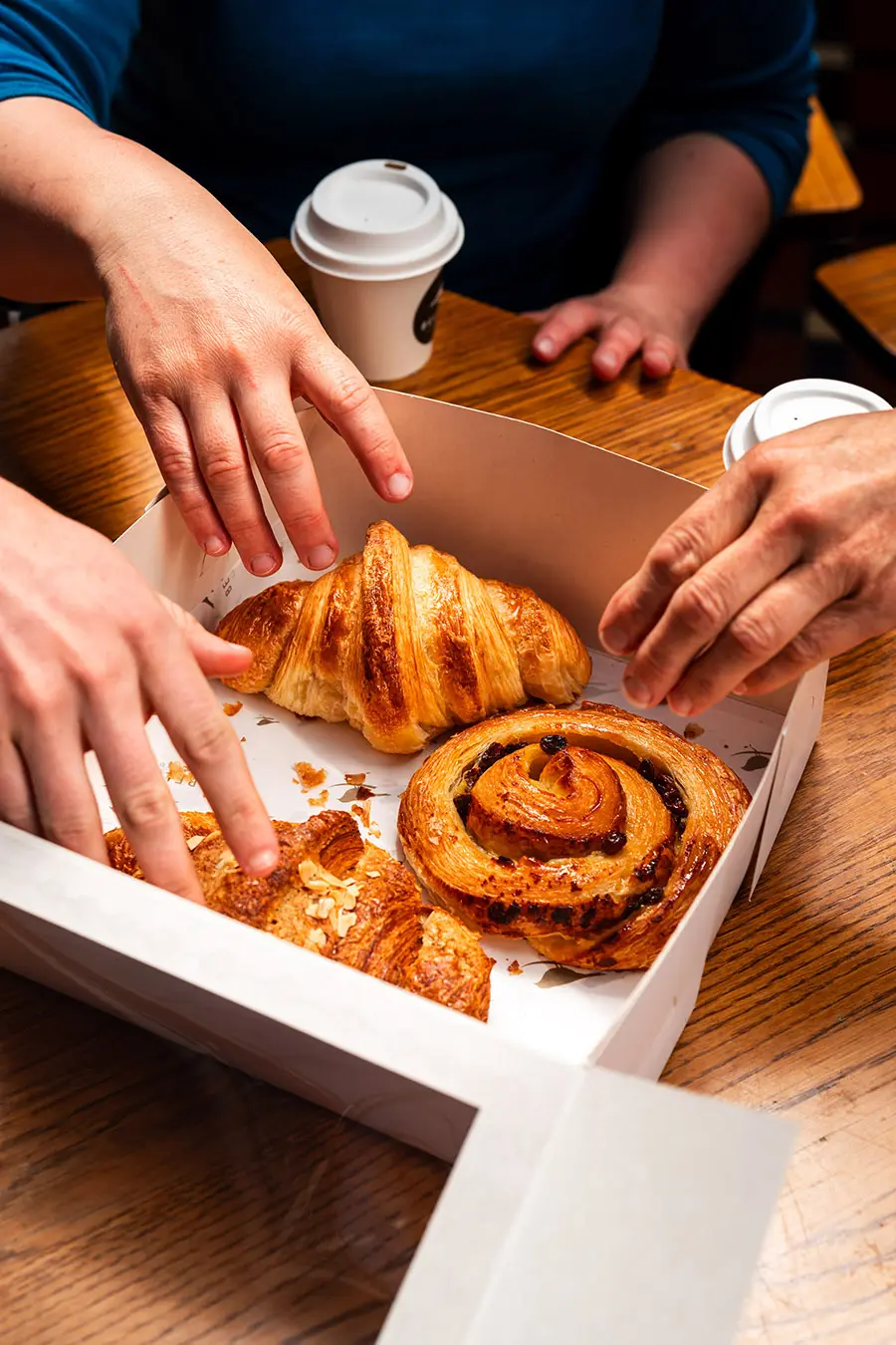 The Classic Box with hands grabbing pastries with Croissant, Pain Aux Raisins, Almond Croissiant and Mini Fruit Danish