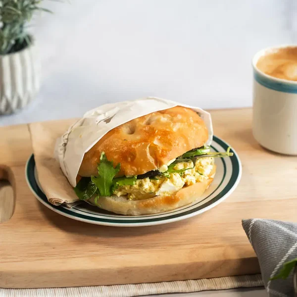 Egg Sandwich on wood board next to coffee cup on white background