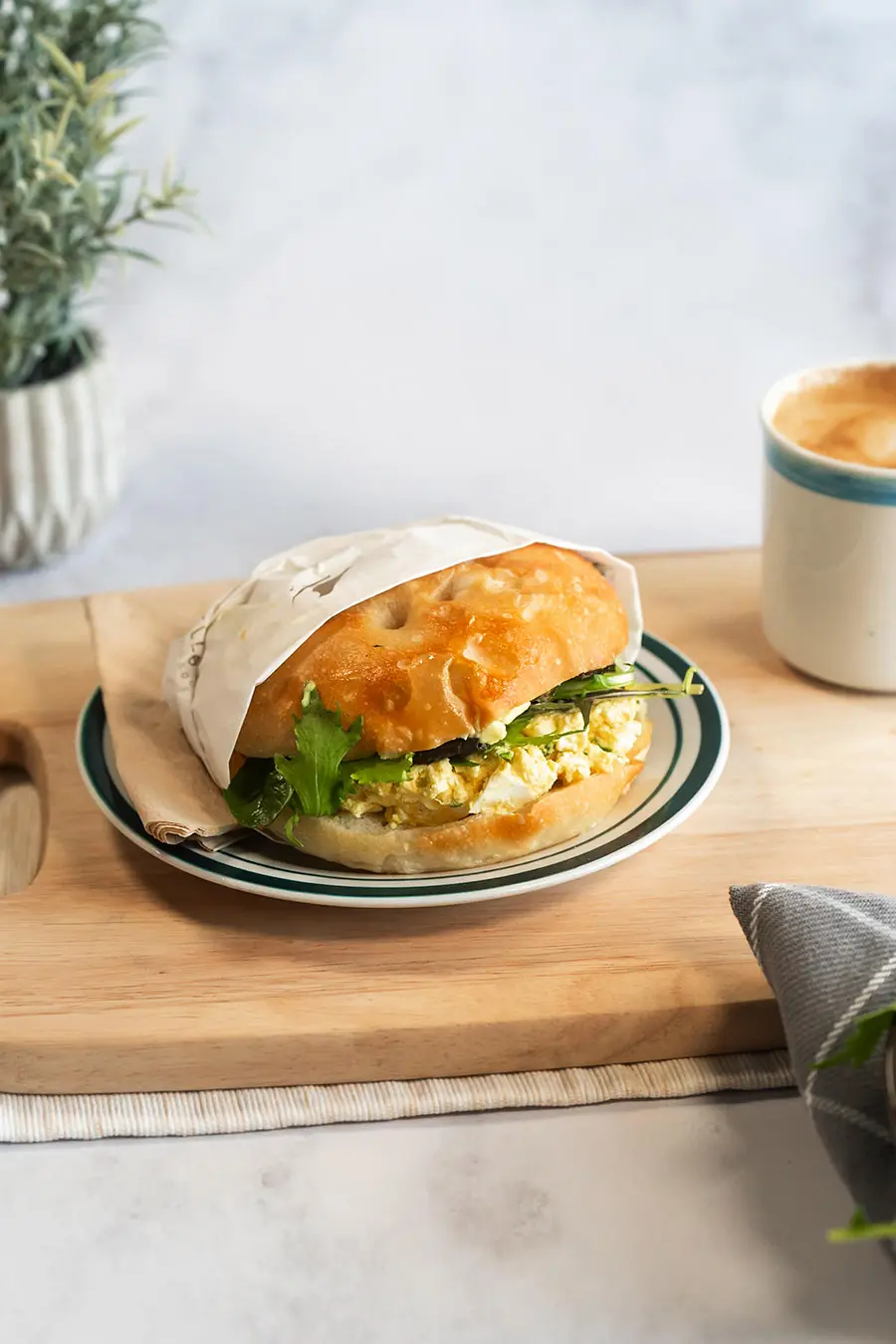 Egg Sandwich on wood board next to coffee cup on white background