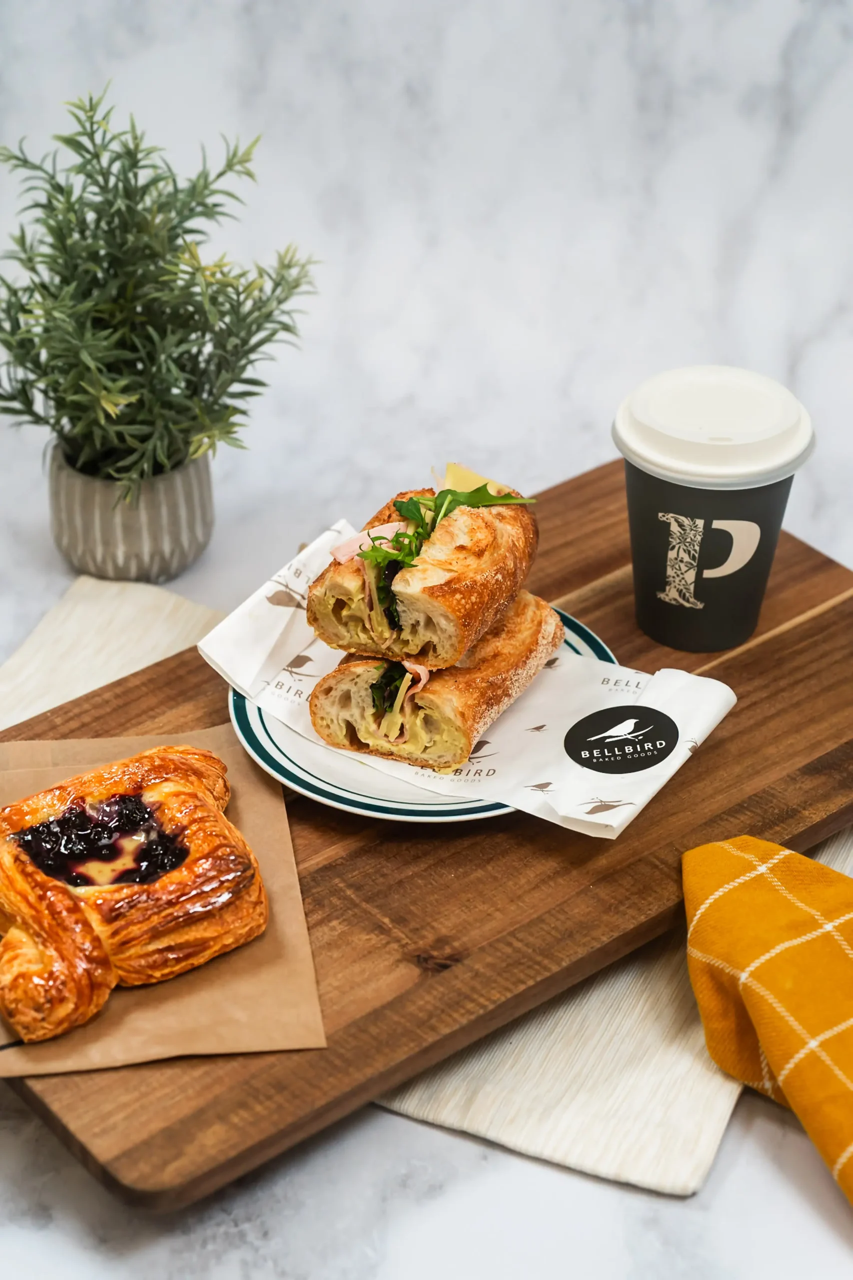 Ham & Cheese Baguette cut in half in open Bellbird Bakery Wrapper on Board