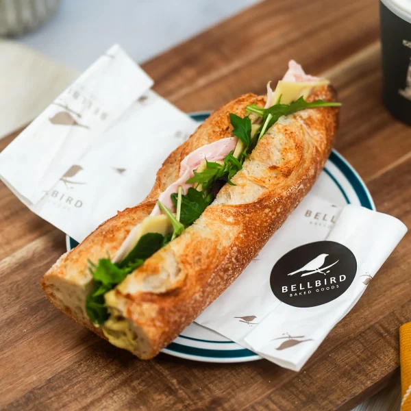 Ham & Cheese Baguette in Open Bellbird Bakery Wrapper on Board