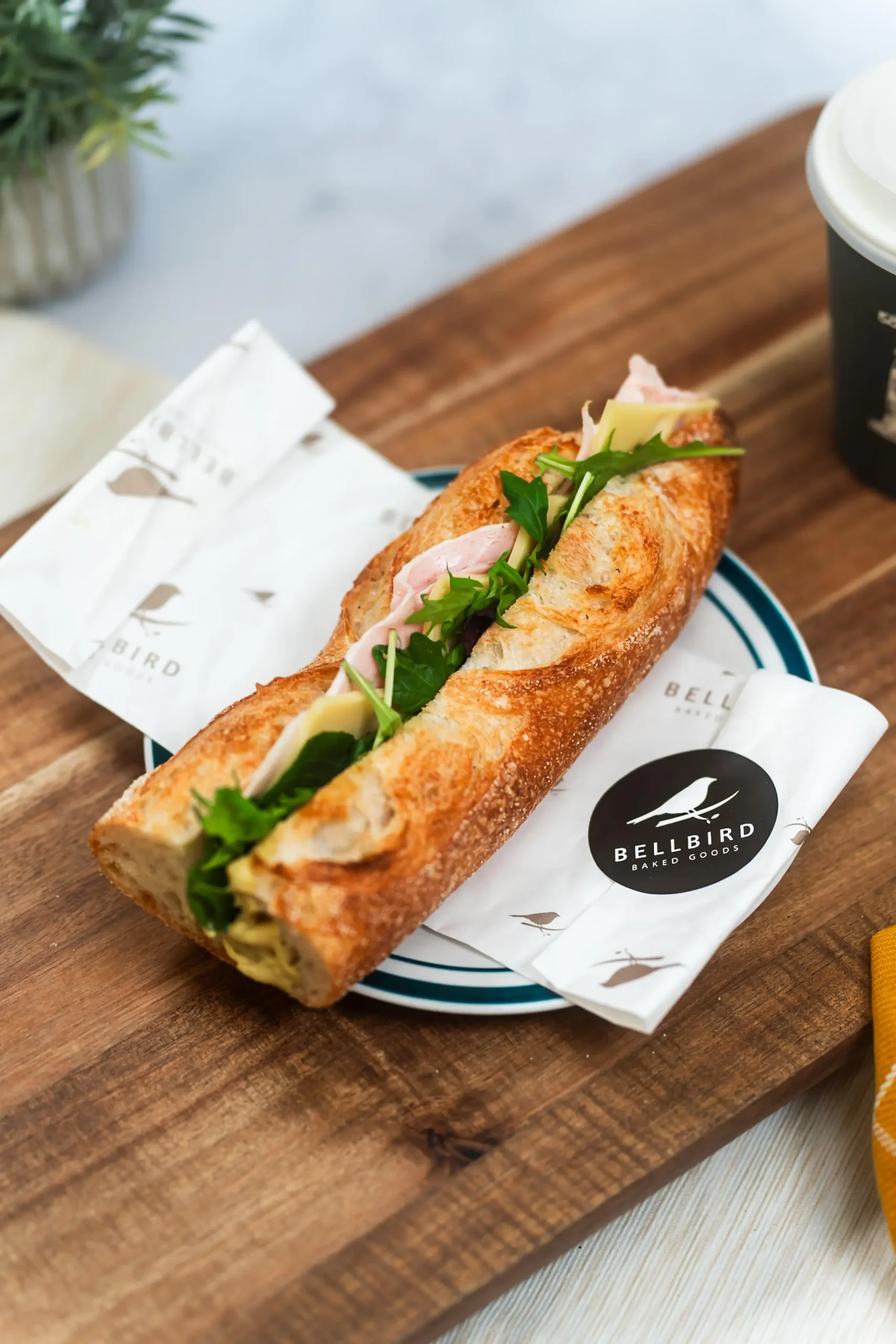 Ham & Cheese Baguette in Open Bellbird Bakery Wrapper on Board