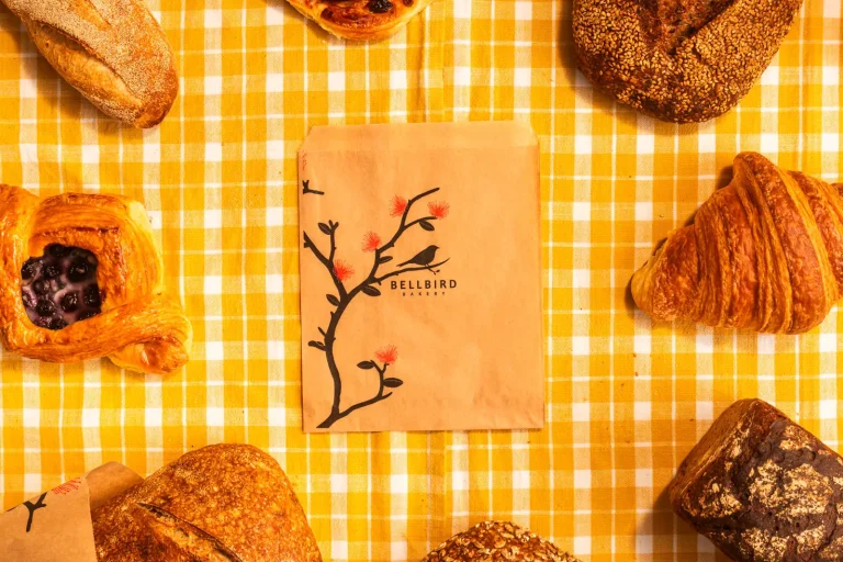 A Bellbird paper bag surrounded by pastries and loaves