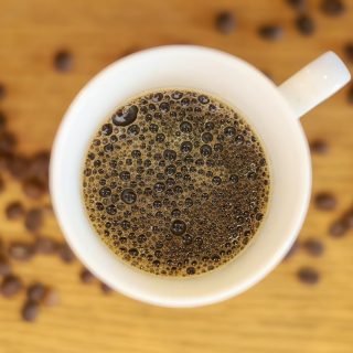 Prima black Filter Coffee in a cup with scattered beans seen from above