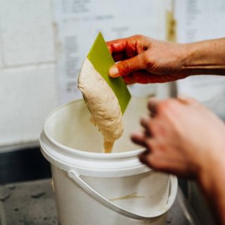 Sourdough starter being weighed up in white bucket with dough cutter